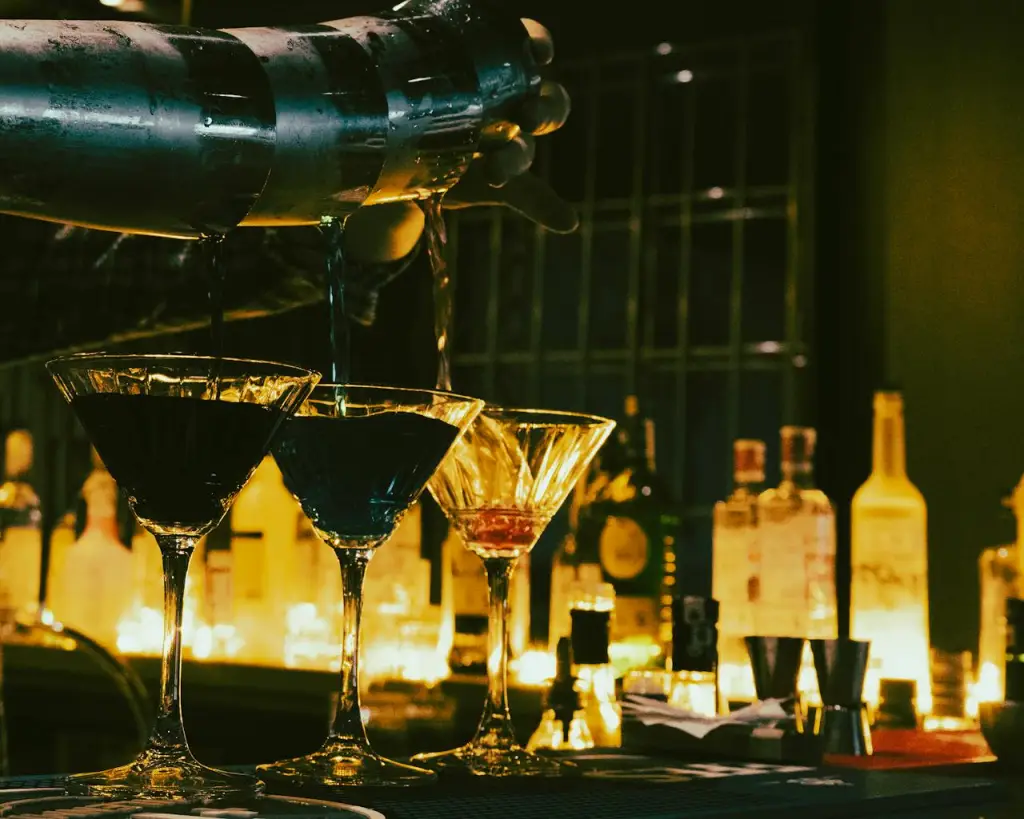 Bartender pouring cocktails in a dimly lit bar, emphasizing mixology and nightlife ambiance.
