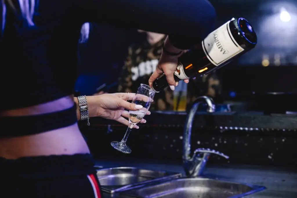 A person pouring champagne into a glass in a dimly lit bar setting.